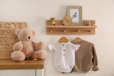 Wooden shelf with baby clothes, toys and furniture in room. Interior design