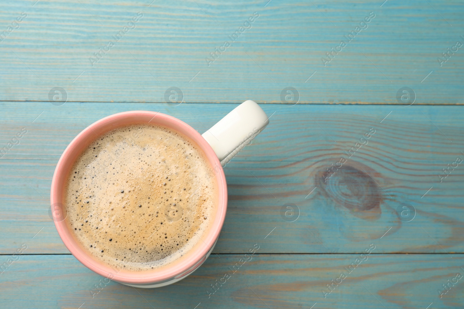 Photo of Cup of aromatic coffee on light blue wooden table, top view. Space for text