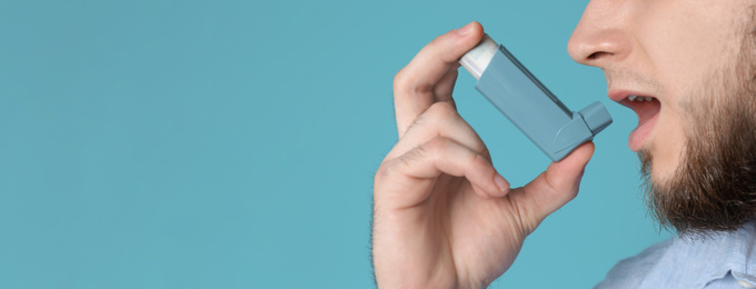 Image of Closeup view of man using asthma inhaler on blue background, space for text. Banner design