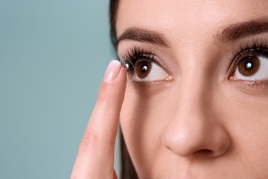 Photo of Young woman putting contact lens in her eye on color background
