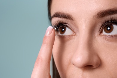 Young woman putting contact lens in her eye on color background