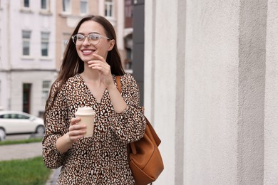 Young woman with cup of drink walking on city street, space for text