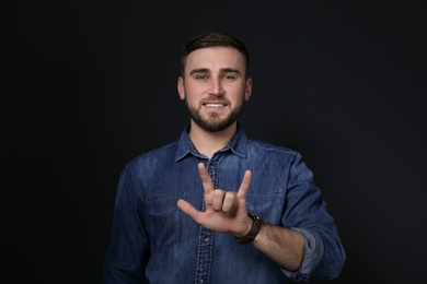 Photo of Man showing I LOVE YOU gesture in sign language on black background