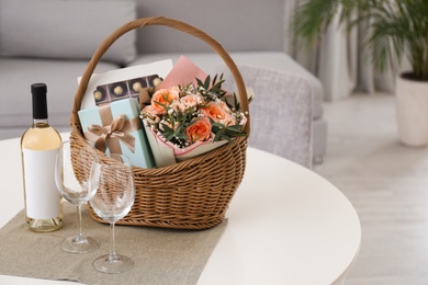Wicker basket with gifts near bottle of wine and glasses on table indoors. Space for text