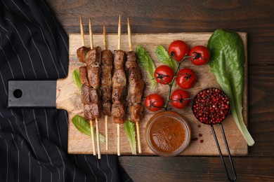 Photo of Tasty cooked marinated meat served with sauce and tomatoes on wooden table, flat lay