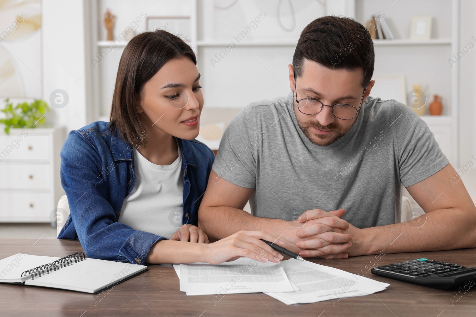 Photo of Young couple with papers discussing pension plan at wooden table indoors