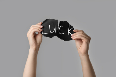Photo of Woman tearing black paper with word LUCK on light grey background, closeup