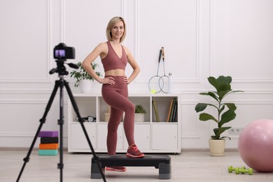 Photo of Smiling sports blogger recording fitness lesson with camera at home