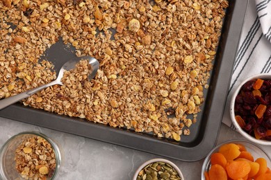 Photo of Making granola. Baking tray with mixture of oat flakes, other ingredients and spoon on grey marble table, flat lay