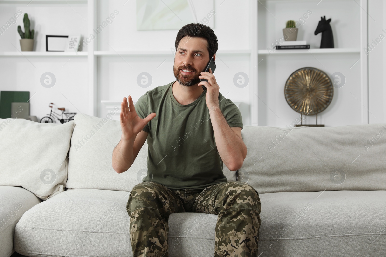 Photo of Happy soldier talking on phone in living room. Military service