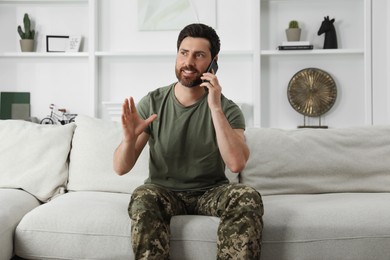 Photo of Happy soldier talking on phone in living room. Military service