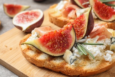 Bruschettas with cheese, prosciutto and figs served on wooden board, closeup