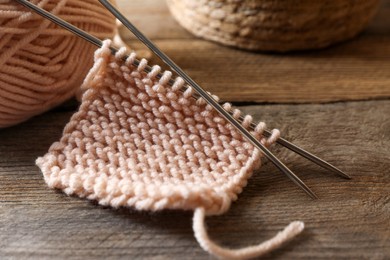 Photo of Soft beige knitting and metal needles on wooden table, closeup