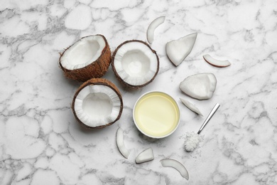 Bowl of natural organic oil and coconuts on marble background, flat lay