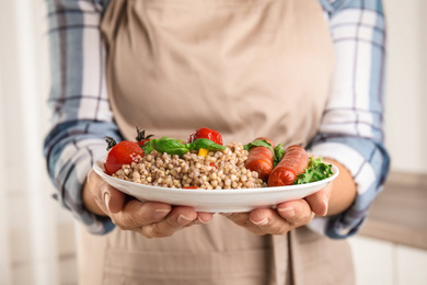 Photo of Woman holding plate with tasty buckwheat porridge and sausages, closeup