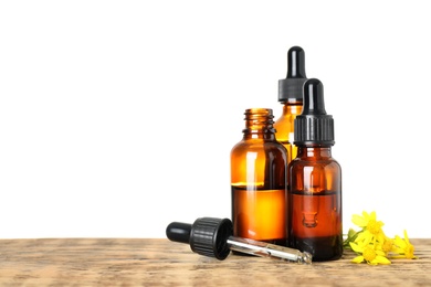 Bottles of essential oil and flowers on wooden table, white background