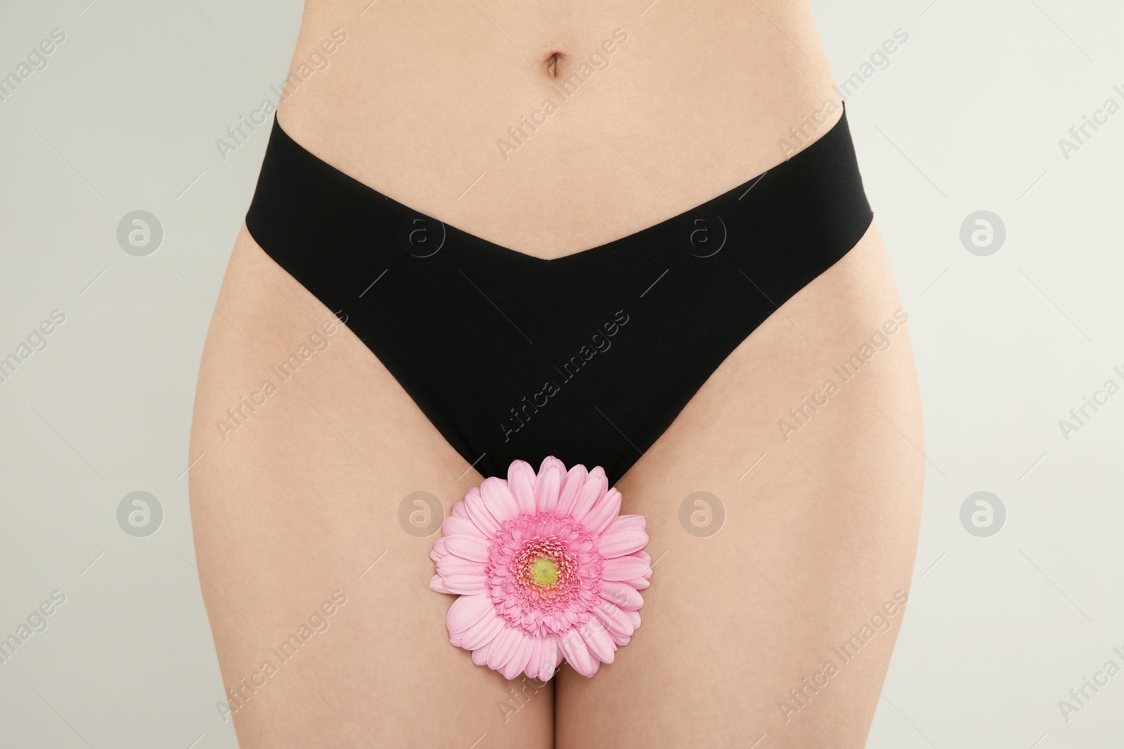 Photo of Gynecology. Woman in underwear with gerbera flower on light background, closeup