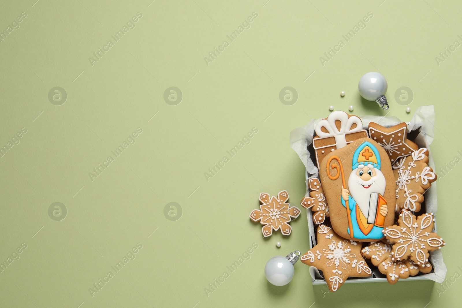 Photo of Tasty gingerbread cookies and Christmas balls on light green background, flat lay with space for text. St. Nicholas Day celebration