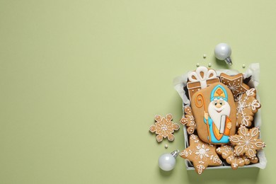 Tasty gingerbread cookies and Christmas balls on light green background, flat lay with space for text. St. Nicholas Day celebration