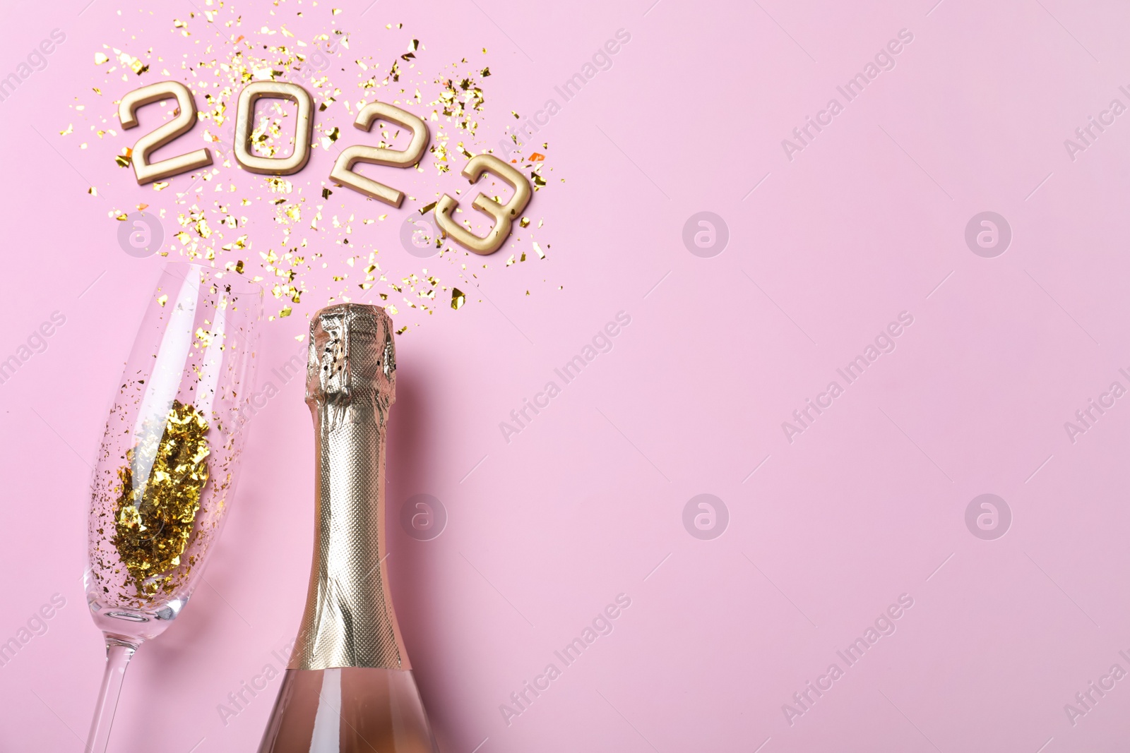 Photo of Bottle of sparkling wine, glass, golden confetti and number 2023 on pink background, flat lay with space for text. Happy New Year