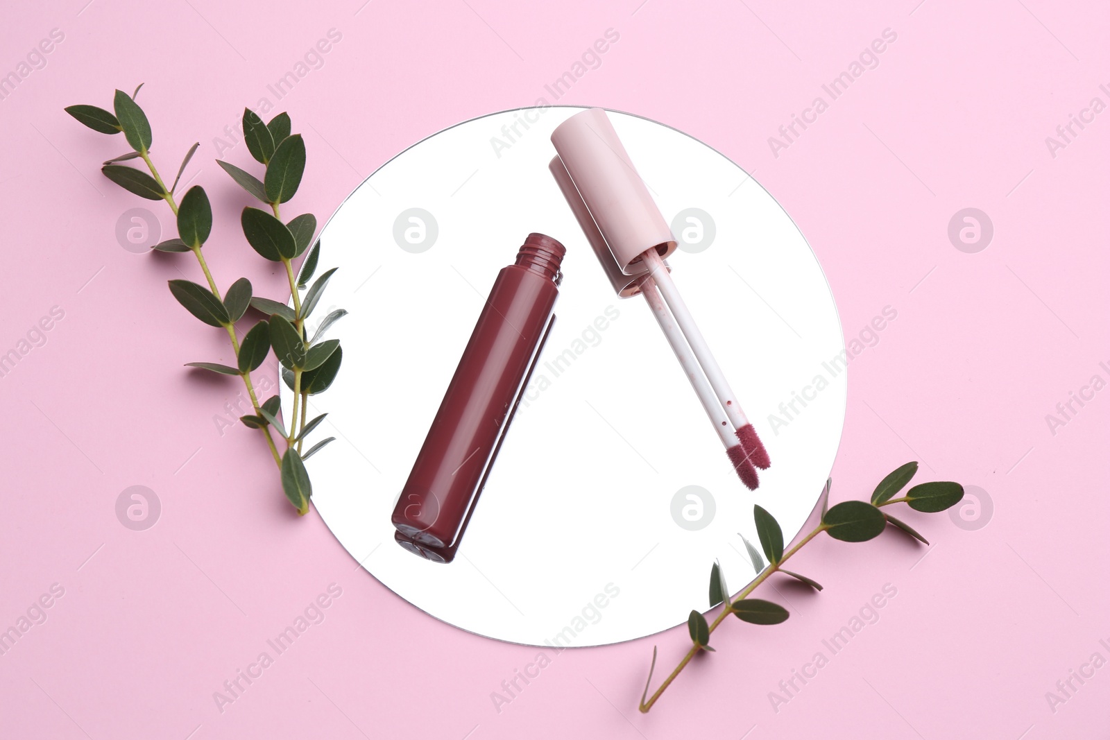 Photo of Lip gloss, green twigs and mirror on pink background, flat lay