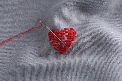 Embroidered red heart and needle on gray cloth, above view