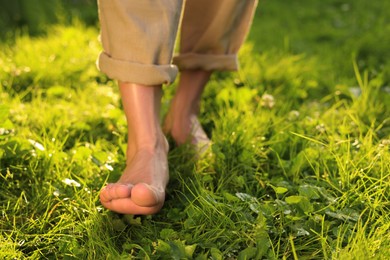 Photo of Woman walking barefoot on green grass outdoors, closeup