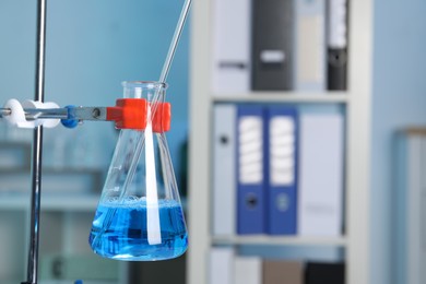 Photo of Laboratory analysis. Glass flask with blue liquid on stand indoors, closeup. Space for text