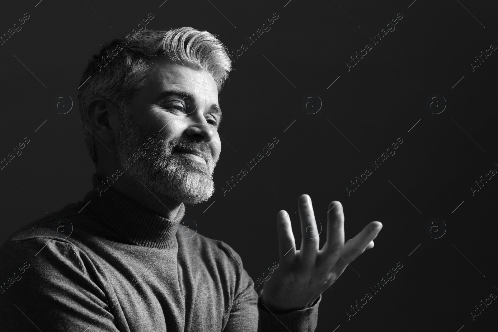 Photo of Portrait of handsome man gesturing on dark background. Black and white effect