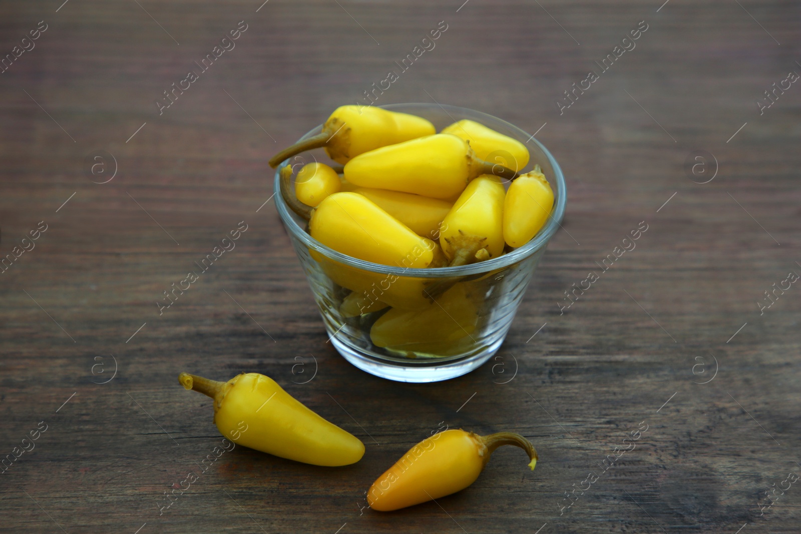 Photo of Glass bowl of pickled yellow jalapeno peppers on wooden table