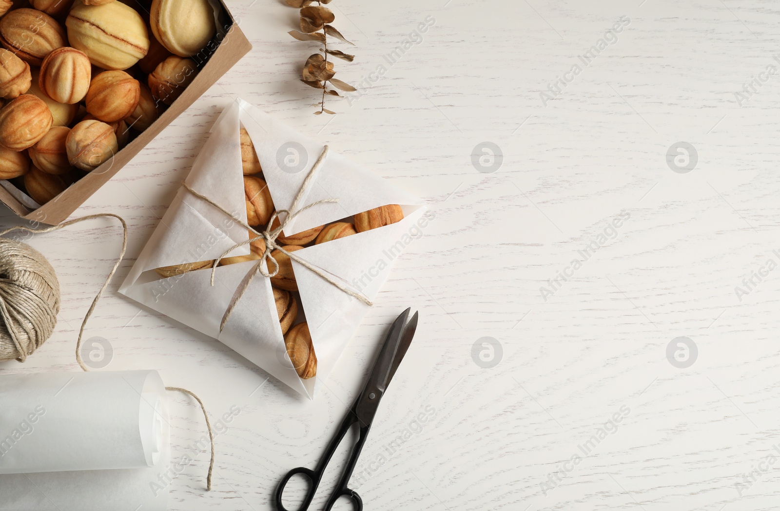 Photo of Walnut shaped cookies filled with caramelized condensed milk on white wooden table, flat lay and space for text. Homemade pastry packed for present