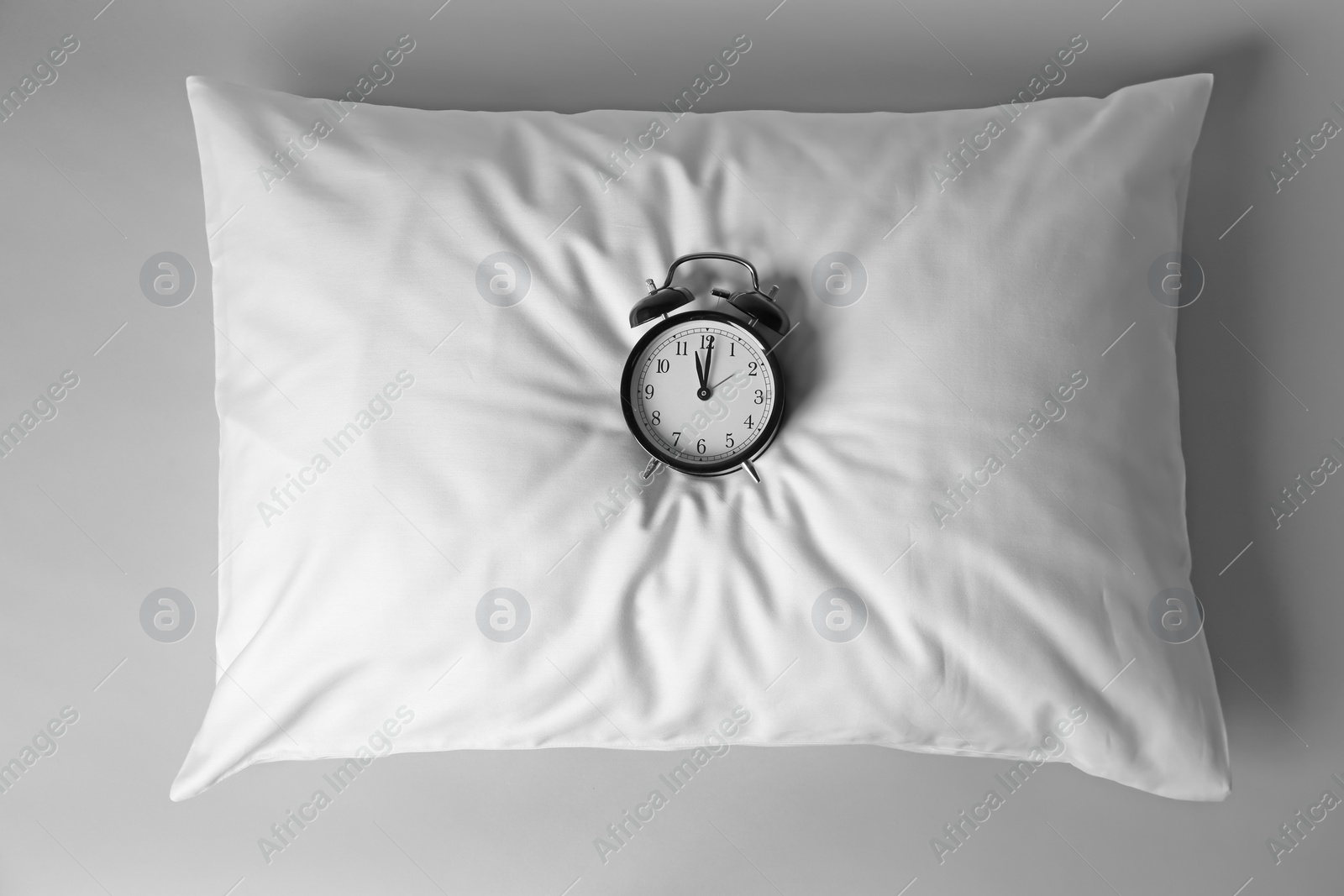 Photo of Blank soft pillow with alarm clock on light background