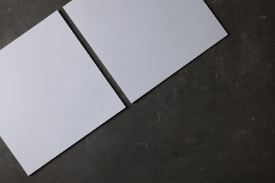 Photo of Blank paper sheets on dark textured background, top view. Mockup for design