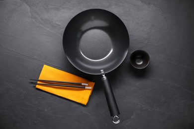 Empty iron wok, sauce bowl and chopsticks on black table, flat lay