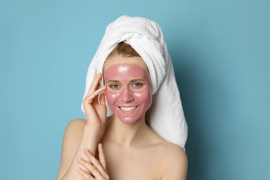 Young woman with pomegranate face mask on light blue background