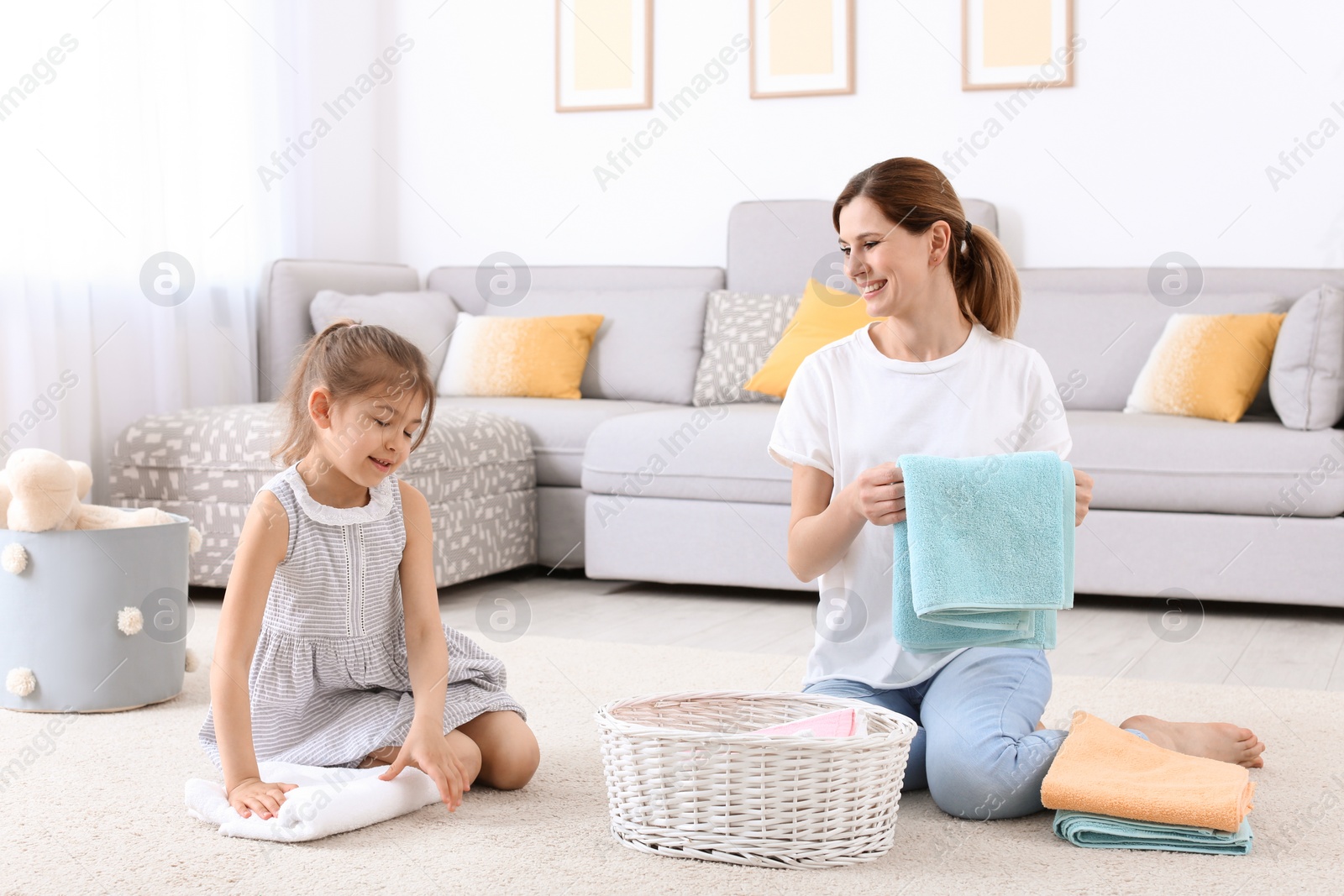 Photo of Housewife with daughter folding freshly washed towels in room