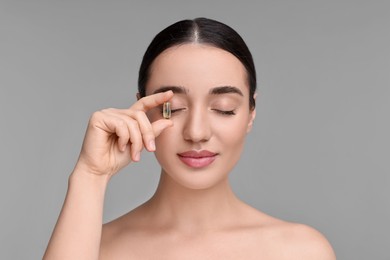 Beautiful young woman with vitamin pill on grey background