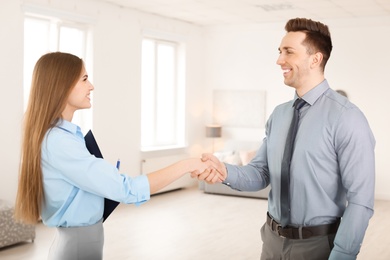 Photo of Beautiful real estate agent and young man shaking hands indoors