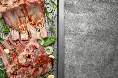 Photo of Raw spare ribs with herbs and seasonings on grey table, top view. Space for text