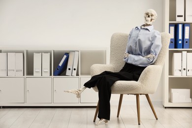 Waiting concept. Human skeleton sitting in armchair at office, space for text