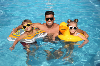 Photo of Happy man and his children with inflatable rings in outdoor swimming pool on sunny summer day