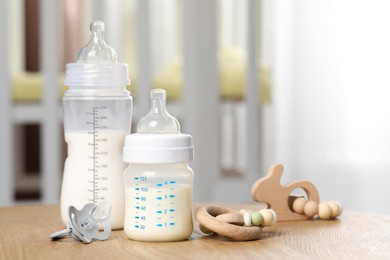 Photo of Feeding bottles with milk, pacifier and toys on wooden table indoors