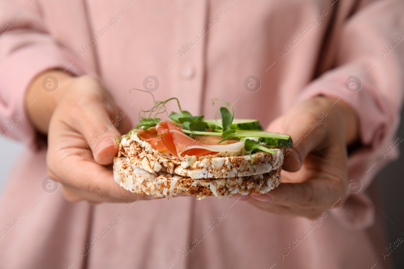 Photo of Woman holding crunchy buckwheat cakes with prosciutto, microgreens and cucumber, closeup
