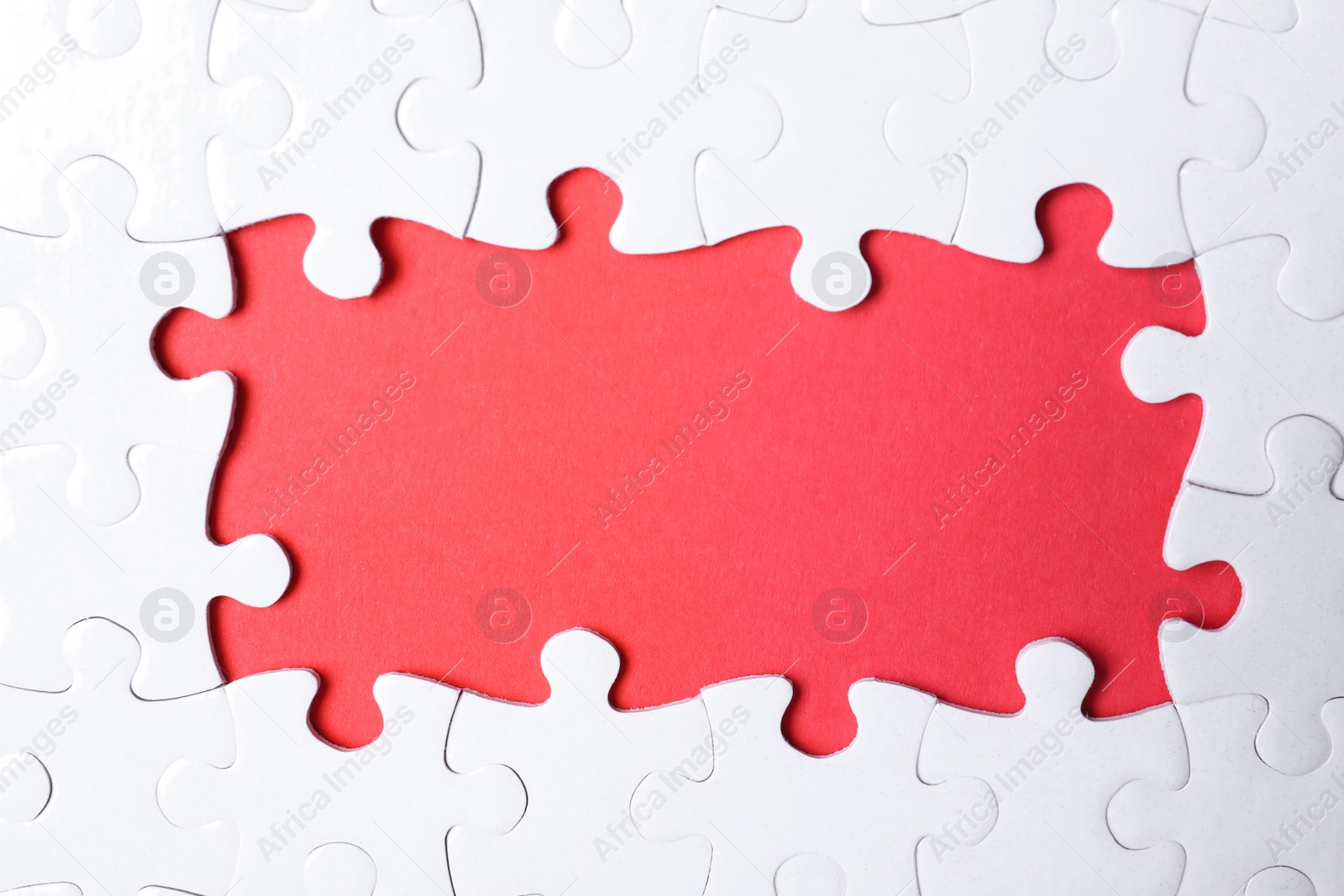Photo of Frame made with white puzzle pieces on red background, top view. Space for text