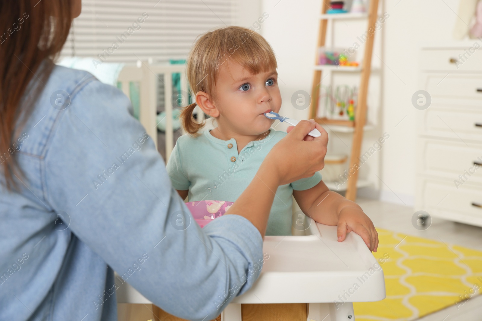 Photo of Mother feeding her cute little child with yogurt at home