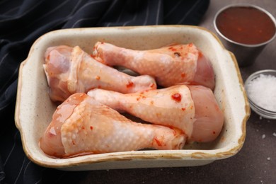 Photo of Fresh marinade and raw chicken drumsticks on brown table, closeup