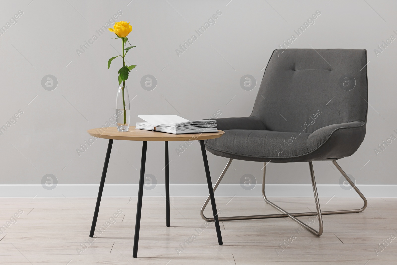 Photo of Comfortable armchair, rose and book on coffee table near light grey wall indoors. Interior design