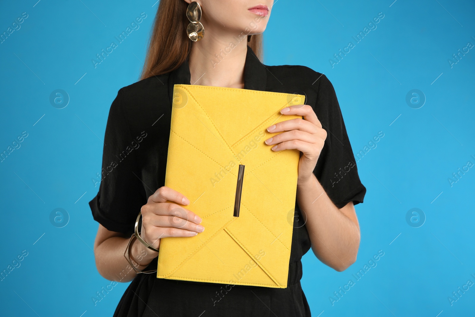 Photo of Young woman with stylish yellow bag on light blue background, closeup