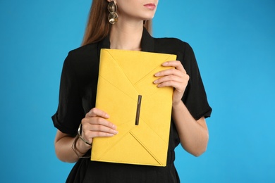 Photo of Young woman with stylish yellow bag on light blue background, closeup