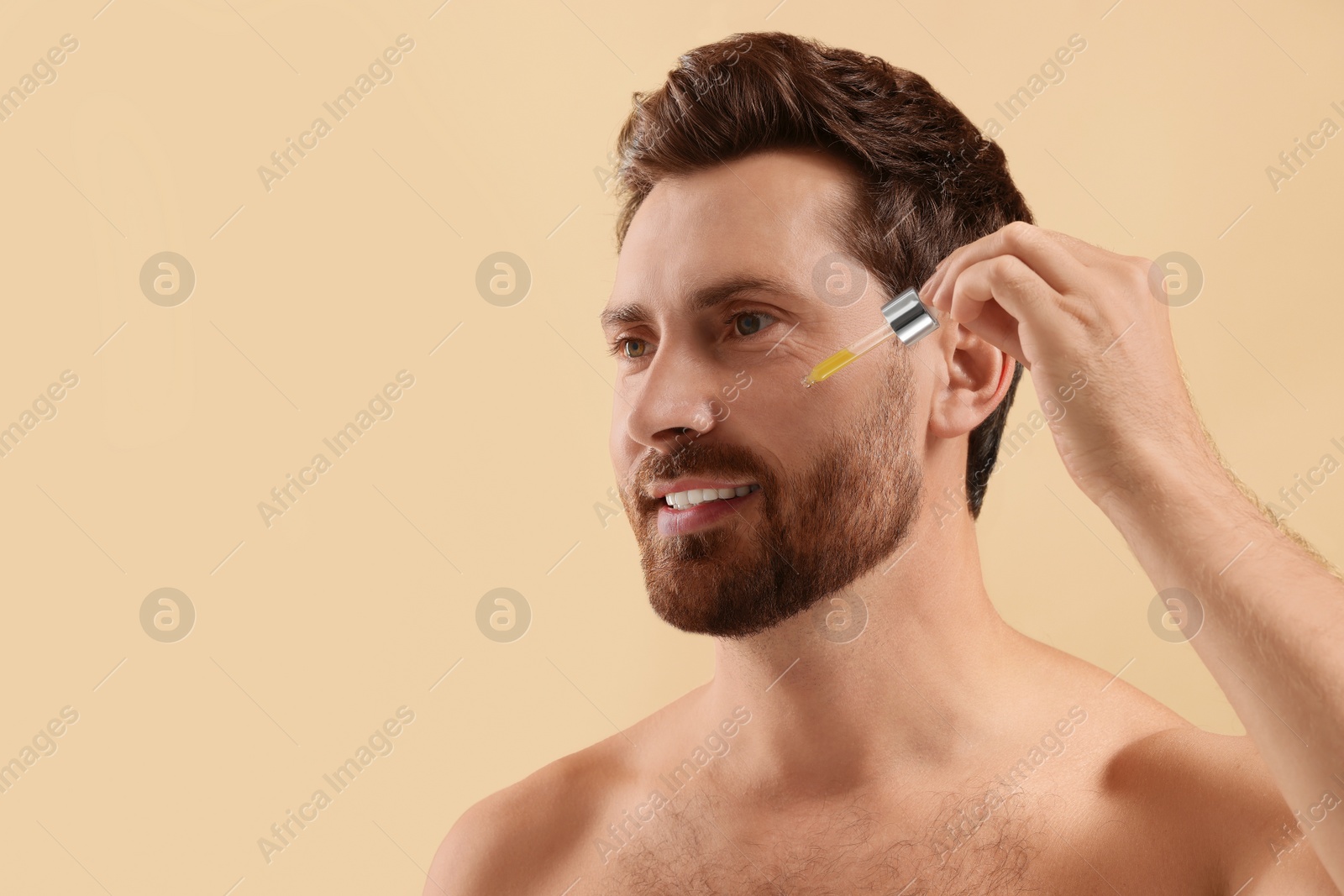 Photo of Smiling man applying cosmetic serum onto his face on beige background, closeup. Space for text